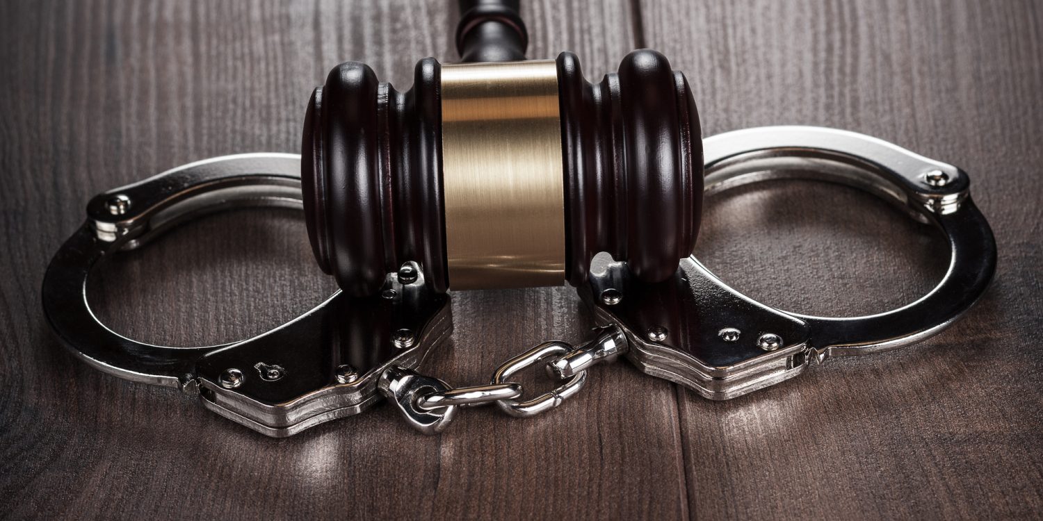 handcuffs and judge gavel on brown wooden table background