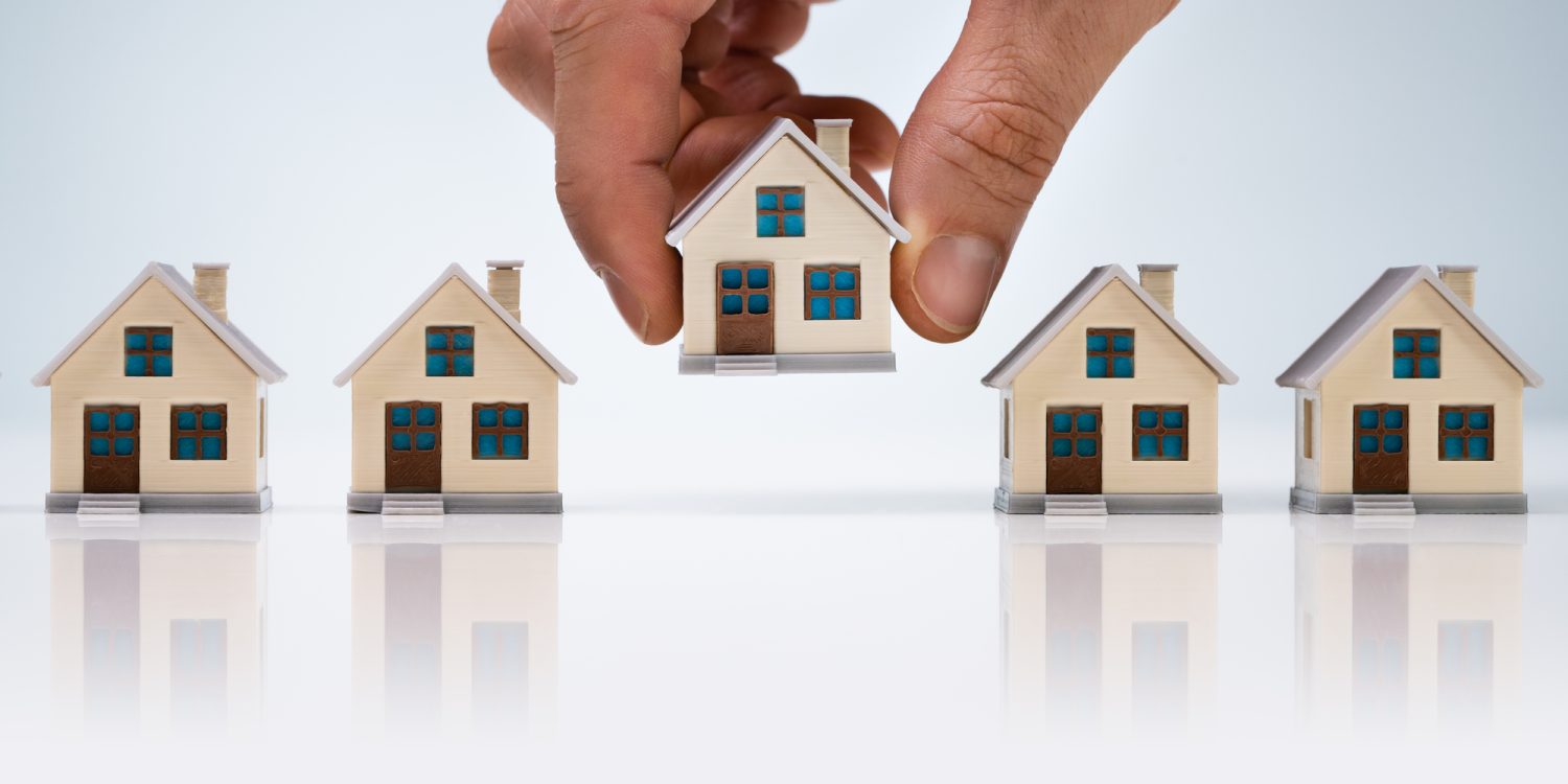Person's Hand Choosing A House Model From The Row Over White Desk